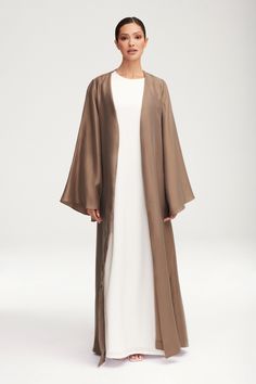 Transform any outfit into a statement with our Seema Flare Sleeve Open Abaya in Taupe. Its luxurious fabric boasts a subtle sheen, while the dramatic flare sleeves add a touch of artful elegance. Step out in style and sophistication with this exclusive piece. Model is 5'7" and is wearing size XS/58". Abaya Inspiration, Khaleeji Abaya, Abaya Outfit, Moslem Fashion, Open Abaya, Hijab Trends, Muslim Women Fashion, Flowy Design, Satin Long Sleeve