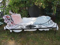 a wrought iron bed with two pillows on it in the grass next to some trees