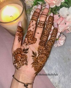 a woman's hand with henna on it next to flowers and a candle