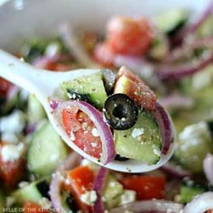 a white spoon filled with cucumber, tomato and onion salad on top of a table