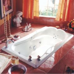 a bath tub sitting on top of a tiled floor next to a vase with flowers