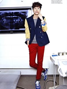 a man standing in front of a white wall wearing red pants and a blue vest