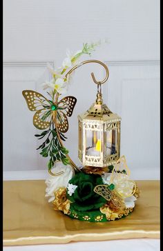 a decorative lantern with flowers and butterflies on the top is sitting on a gold table cloth