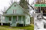 the house is green and has a woman in front with her mouth open next to a street sign