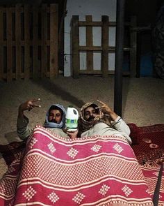 two people are laying on a blanket and pointing at something in the air with their hands