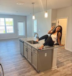 a beautiful woman sitting on top of a kitchen counter next to a sink and oven