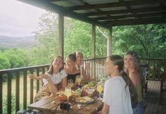 a group of women sitting at a table on top of a wooden deck next to trees