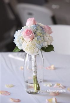 a bouquet of white and pink flowers in a vase on a table with rose petals