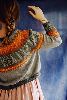 a woman wearing a sweater with an orange and green design on the back, standing in front of a blue backdrop