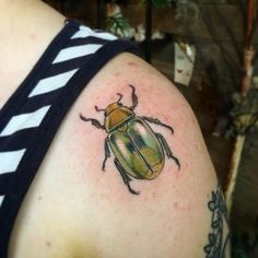 a beetle tattoo on the back of a woman's shoulder, it is green and yellow