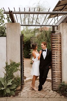 a man and woman standing in front of a wooden structure with an open door that leads into the back yard