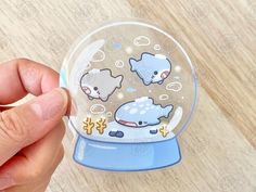 a hand holding a snow globe with animals on it and bubbles in the air,