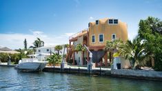 there is a house on the water with boats in front and palm trees around it