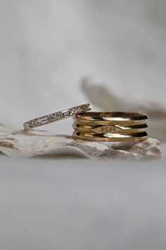 three gold wedding rings with diamonds on top of each other, sitting on a piece of driftwood