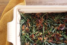 green beans and mushrooms in a white casserole dish on a yellow towel next to a wooden table