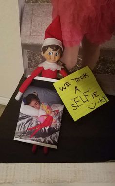 an elf with a sign on the table next to a photo and a note that says we took a selfie