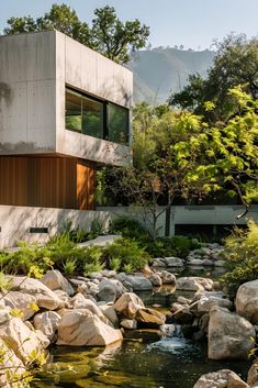 the house is surrounded by rocks and greenery, with a stream running through it