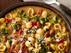 a bowl filled with pasta and spinach on top of a table next to silverware