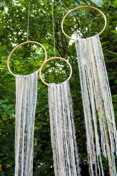 two metal hoop hanging from a tree with white yarn and gold rings on it's sides