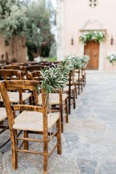 rows of wooden chairs with plants on them in front of an old church door and stone floor