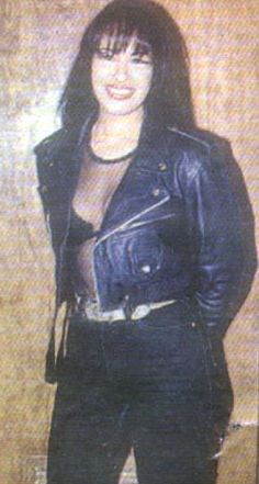 a woman in black leather jacket standing next to a wall