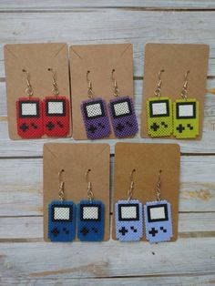 four pairs of pixel earrings are displayed on a wooden table next to a piece of cardboard