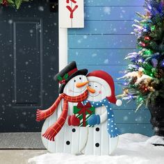 two snowmen standing next to each other in front of a blue house with christmas decorations