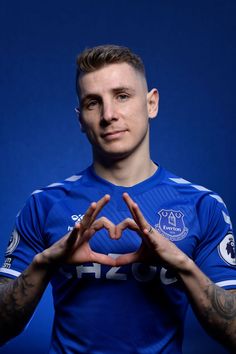 a man making a heart shape with his hands in front of him, against a blue background