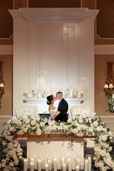 a bride and groom kissing in front of an altar with white flowers, candles and greenery