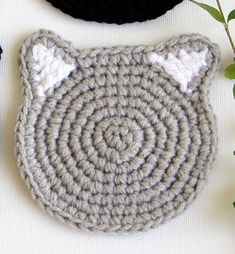 two crocheted cat coasters sitting on top of a table next to a plant