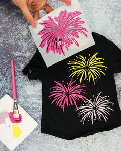 someone is holding up a t - shirt that has fireworks on it and paintbrushes next to it