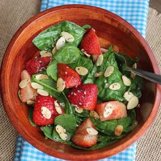 spinach salad with strawberries and almonds in a wooden bowl on a blue checkered tablecloth