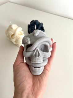 a hand holding a skull candle with two candles in the background