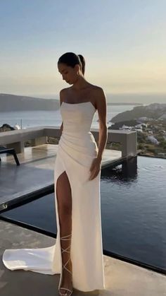 a woman standing on top of a roof next to a pool wearing a white dress