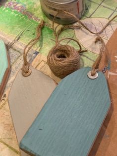 two wooden tags tied to twine on top of a piece of paper next to a can of paint