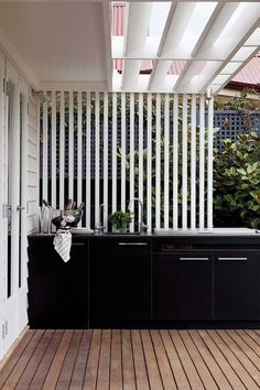 an outdoor kitchen with wooden flooring and black cabinetry on the outside side of the house