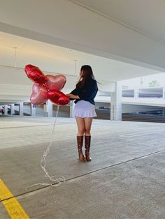 a woman is standing in an empty parking garage holding onto some red heart shaped balloons