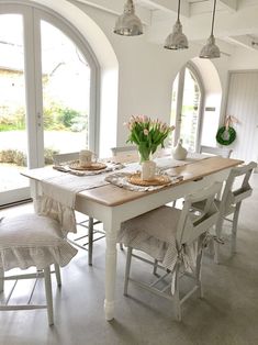 a dining room table and chairs with flowers in vases on the top, next to an arched window