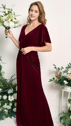 a woman in a long burgundy dress holding a bouquet of flowers and posing for the camera