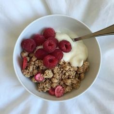 a bowl filled with granola and raspberries on top of a white sheet