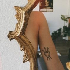 a woman's leg with a tattoo on it and a gold mirror behind her