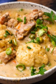 a white bowl filled with meat and dumplings covered in gravy on top of a wooden table