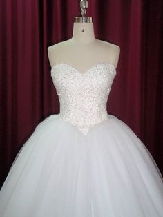 a white wedding dress on display in front of a red curtained background with a mannequin