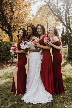 four bridesmaids in red dresses posing for a photo with their bouquets on the grass