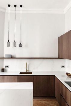 a kitchen with wooden cabinets and white counter tops, two hanging lights above the sink