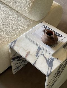 a marble side table with a book on it and a vase sitting on top of it