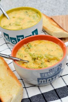 two bowls of broccoli cheese soup on a checkered tablecloth with bread