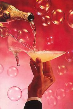 a hand is holding a wine glass and pouring it into a champagne flute with bubbles in the background