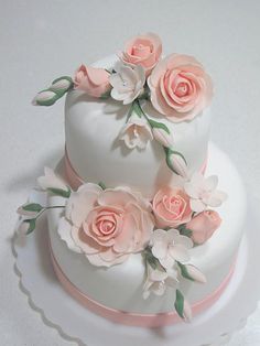 a three tiered cake with pink flowers on the top and white icing around the edges