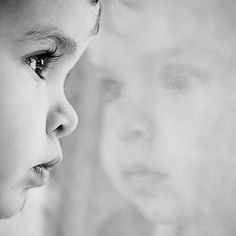 two young children looking at each other in black and white, with one child's face partially obscured by the background